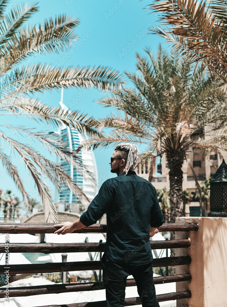 Young man tourist in stylish black clothes and with modern hairstyle is enjoying sightseeing during vacation in Dubai in United Arab Emirates. Luxury and comfortable tourism season in UAE cityscapes Young man tourist in stylish black clothes and with modern hairstyle is enjoying sightseeing during vacation in Dubai in United Arab Emirates. Luxury and comfortable tourism season in UAE cityscapes