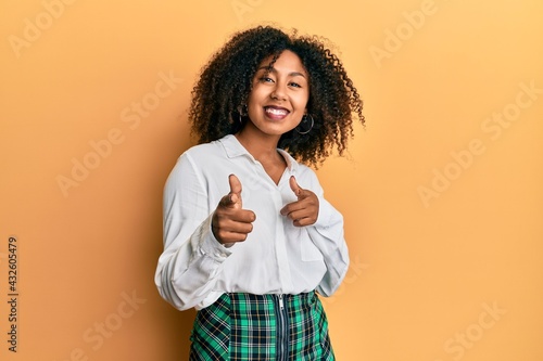 Beautiful african american woman with afro hair wearing scholar skirt pointing fingers to camera with happy and funny face. good energy and vibes.