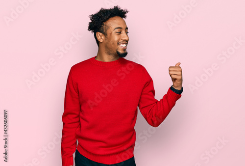Young african american man with beard wearing casual winter sweater smiling with happy face looking and pointing to the side with thumb up.