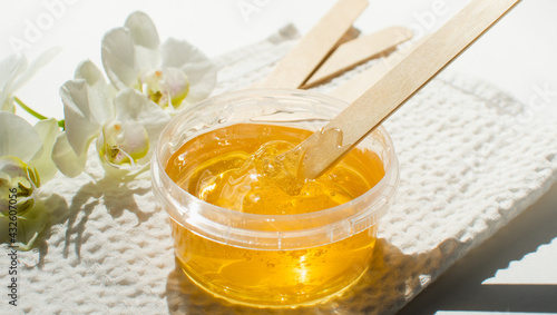 Sugar paste or wax honey in a transparent jar and white orchid on a white background. Sugaring. Depilation and beauty concept. Waxing.