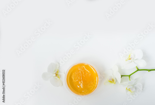 Sugar paste or wax honey in a transparent jar and white orchid on a white background. Sugaring. Depilation and beauty concept. Waxing. Top view. Space for text.