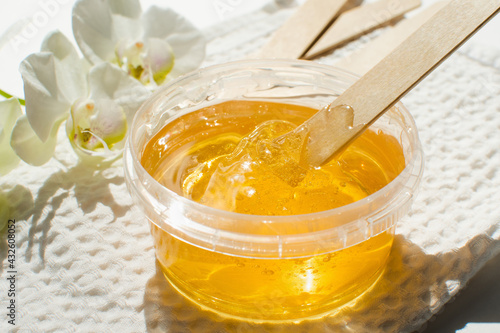 Sugar paste or wax honey in a transparent jar and white orchid on a white background. Sugaring. Depilation and beauty concept. Waxing.