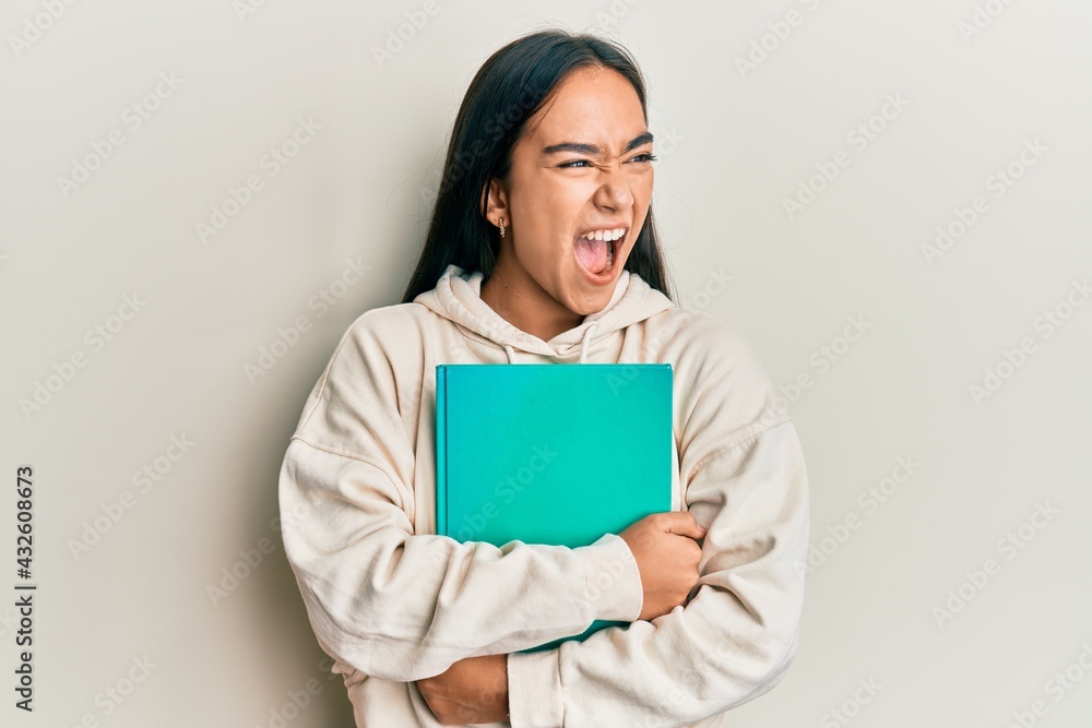Young asian woman holding book angry and mad screaming frustrated and furious, shouting with anger. rage and aggressive concept. Young asian woman holding book angry and mad screaming frustrated and furious, shouting with anger. rage and aggressive concept.