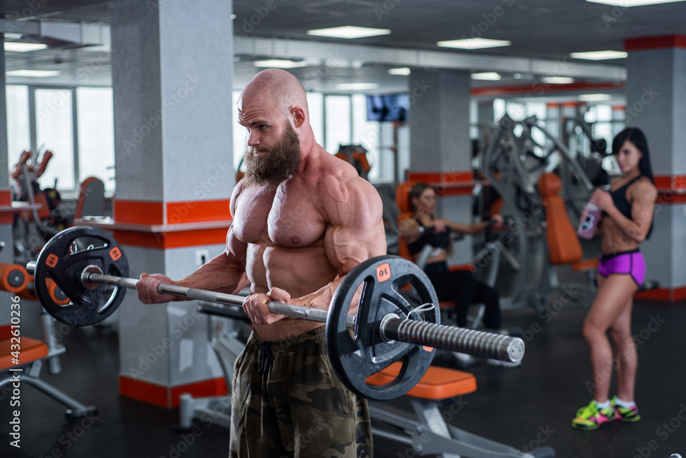 Bald man with a beard in the gym. Muscular bodybuilder guy doing barbell exercises. Strong man with a naked torso. The young athlete is preparing for weightlifting competitions. Bald man with a beard in the gym. Muscular bodybuilder guy doing barbell exercises. Strong man with a naked torso. The young athlete is preparing for weightlifting competitions.