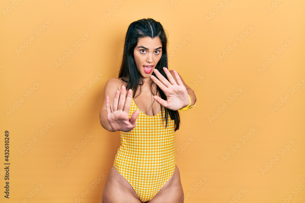 Young hispanic girl wearing swimsuit moving away hands palms showing refusal and denial with afraid and disgusting expression. stop and forbidden. Young hispanic girl wearing swimsuit moving away hands palms showing refusal and denial with afraid and disgusting expression. stop and forbidden.