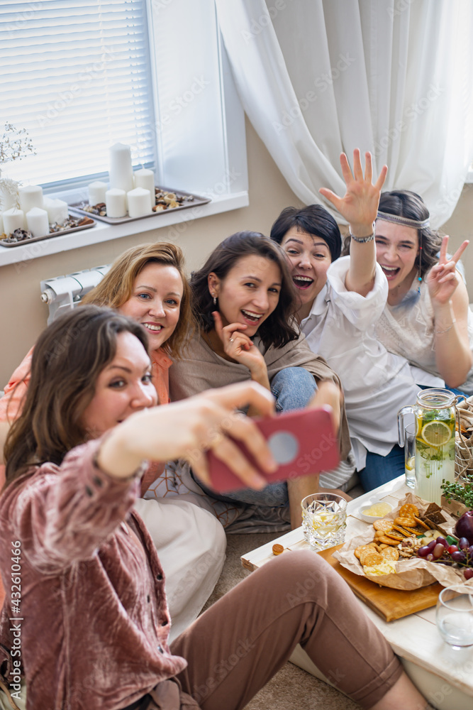 Obraz premium Group of happy young female friends posing taking selfie use smartphone at hen-party in hippie style