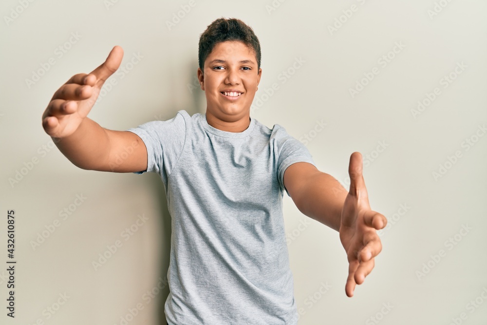Teenager hispanic boy wearing casual grey t shirt looking at the camera smiling with open arms for hug. cheerful expression embracing happiness. Teenager hispanic boy wearing casual grey t shirt looking at the camera smiling with open arms for hug. cheerful expression embracing happiness.