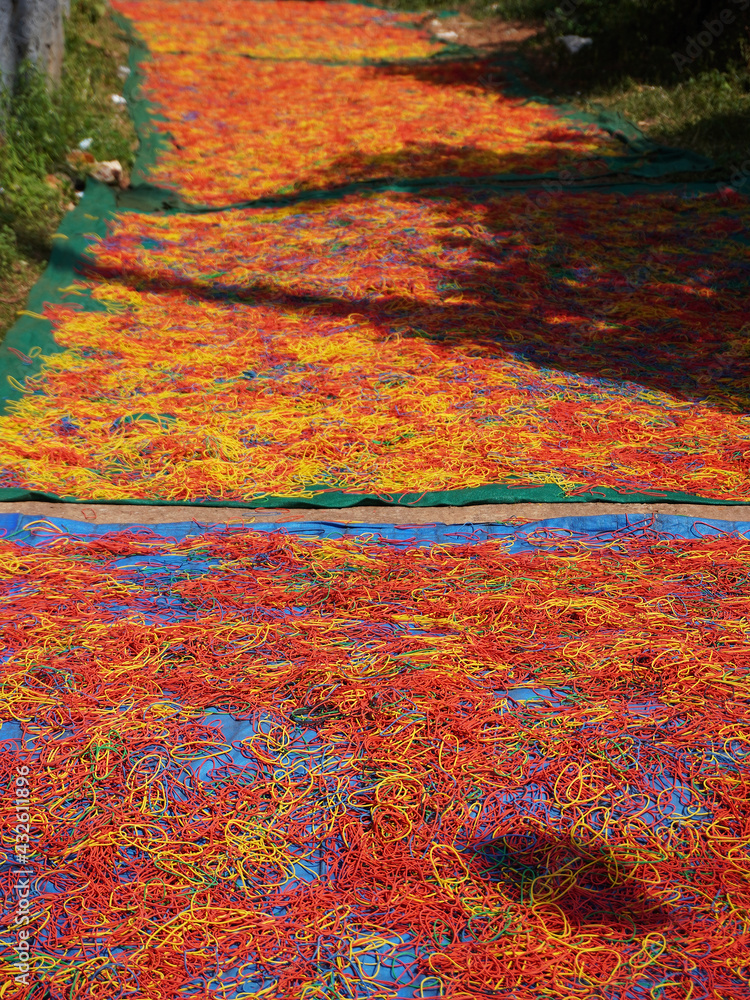 Freshly made rubber bands of different colors being sun dried, spread on the ground.