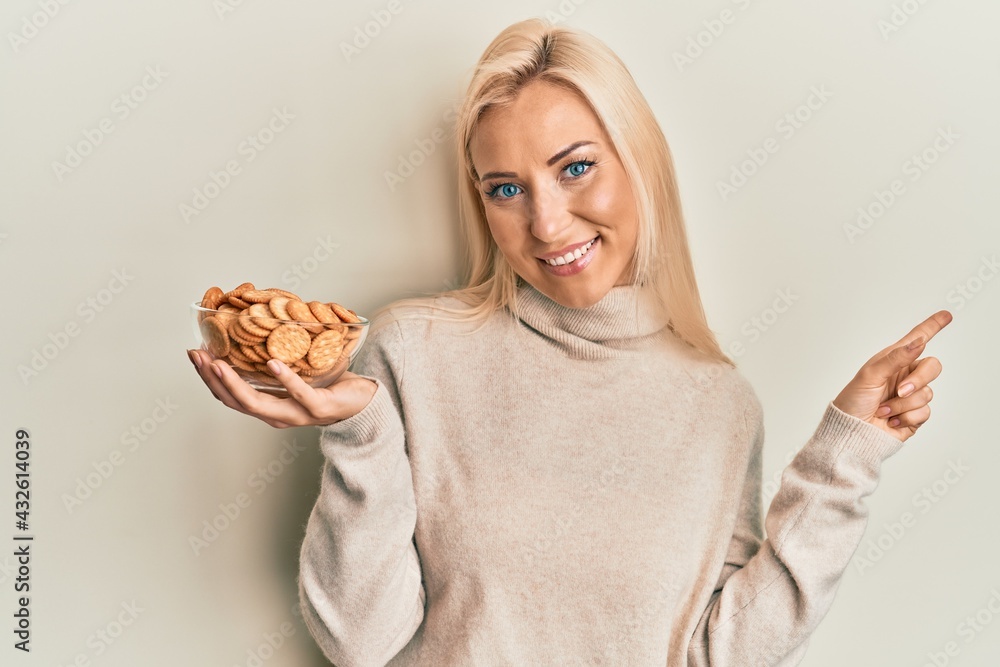 Young blonde woman cooking using baker whisk smiling happy pointing with hand and finger to the side Young blonde woman cooking using baker whisk smiling happy pointing with hand and finger to the side