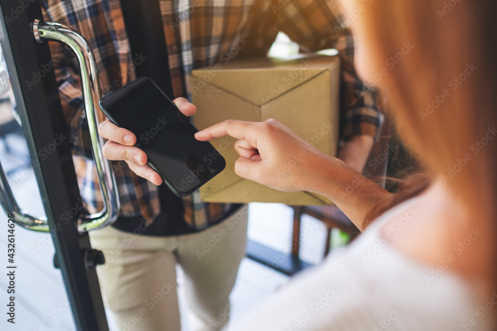 Closeup image of a woman receiving parcel box and signing name on the phone from delivery man at the house's door Closeup image of a woman receiving parcel box and signing name on the phone from delivery man at the house's door