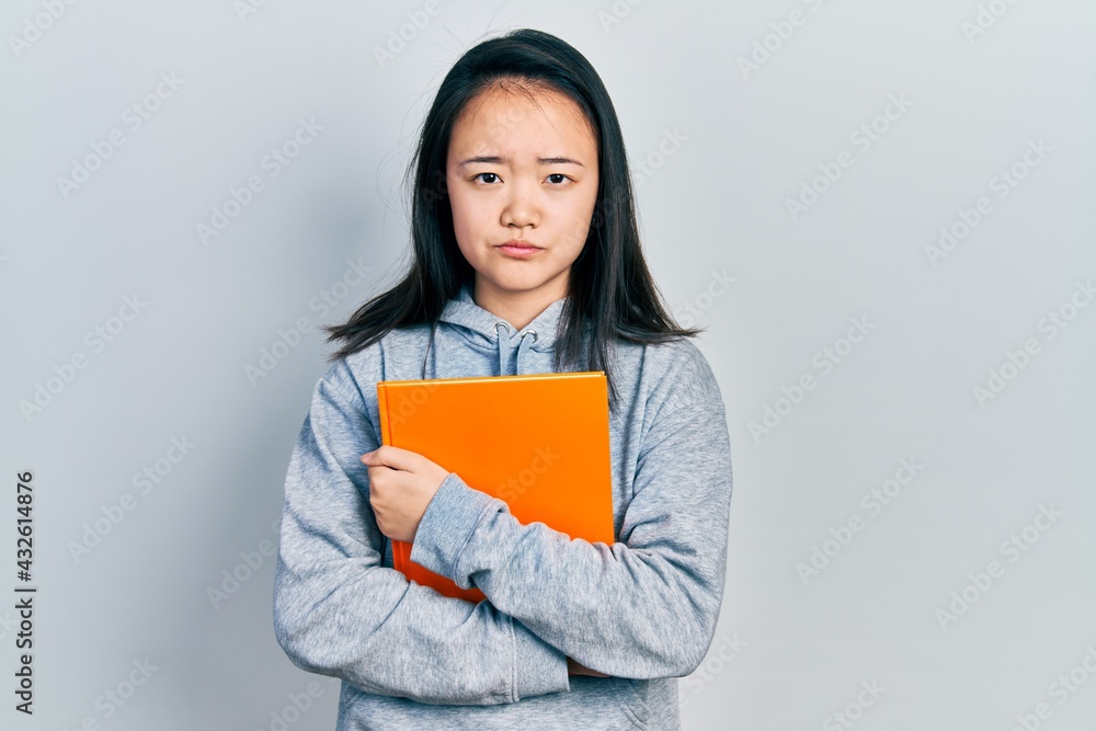 Young chinese girl holding book depressed and worry for distress, crying angry and afraid. sad expression. Young chinese girl holding book depressed and worry for distress, crying angry and afraid. sad expression.