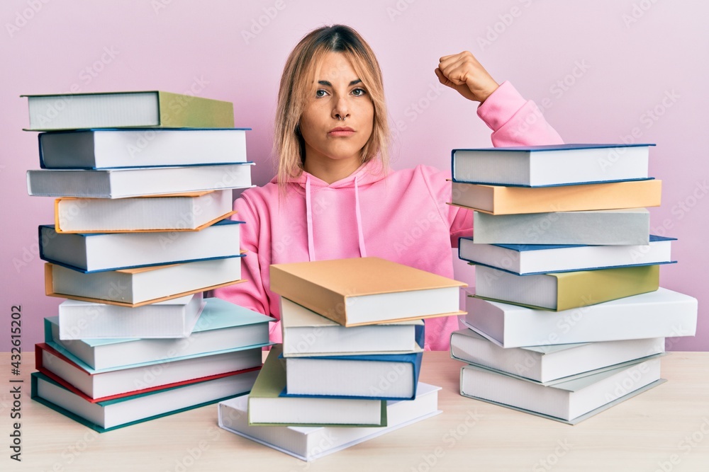 Young caucasian woman sitting on the table with books strong person showing arm muscle, confident and proud of power Young caucasian woman sitting on the table with books strong person showing arm muscle, confident and proud of power
