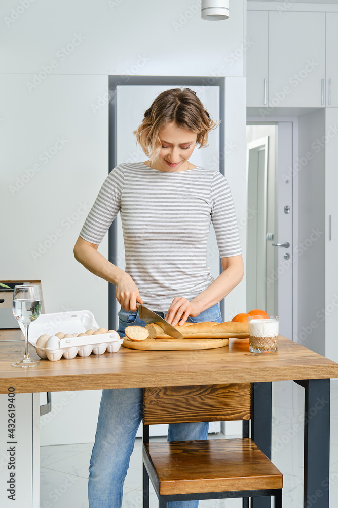 Smiling woman slicing baguette on cutting board in the kitchen Smiling woman slicing baguette on cutting board in the kitchen