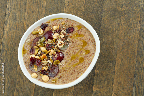 Appetizing flaxseed porridge with olive oil, seeds, grapes and hazelnuts in a white bowl on a wooden background. Vegetarian food. Eastern cuisine