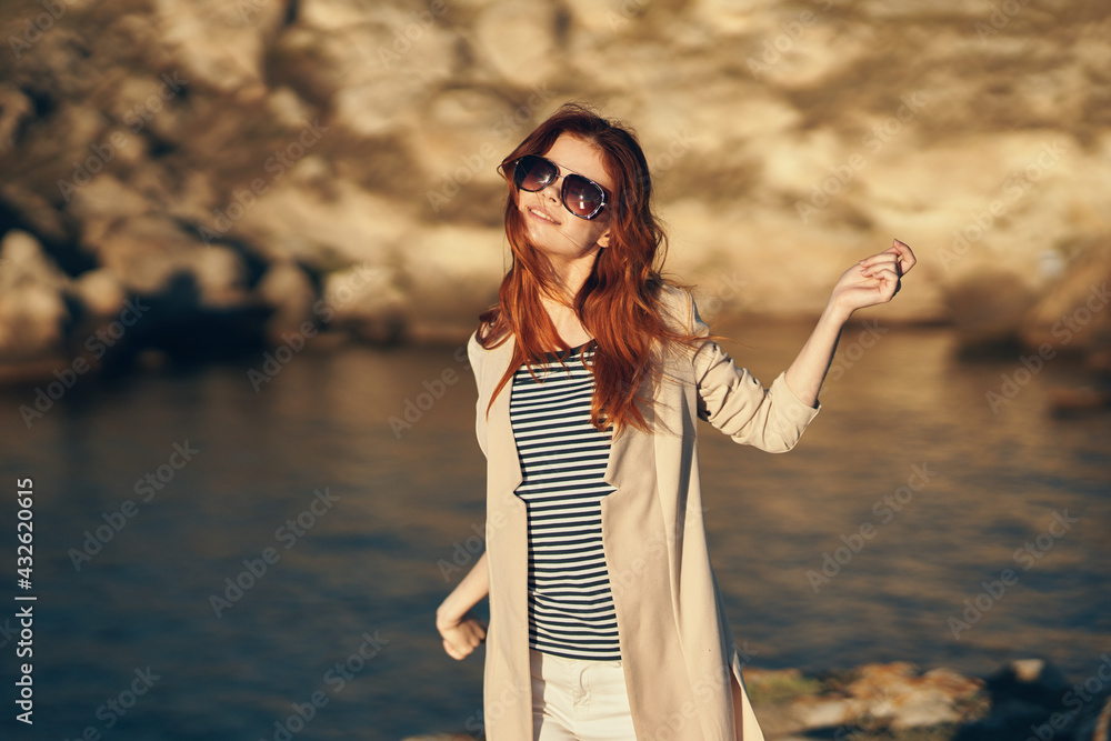 woman in a t-shirt holds her hands above her head near the sea in the mountains woman in a t-shirt holds her hands above her head near the sea in the mountains