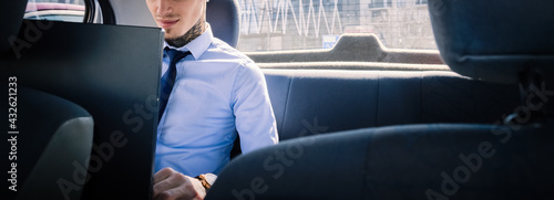 Cropped image of Young entrepreneur with blue shirt and tie is working on a project on the back seat of the car.
