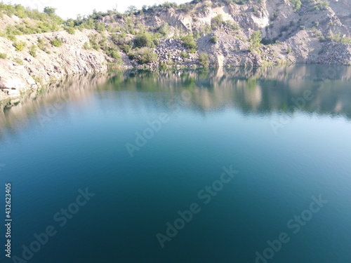 Rocky shore of the Radon Lake on a sunny summer morning. Aerial view of an old flooded granite quarry. A picturesque pond.