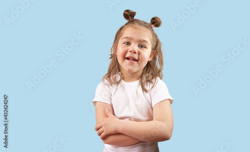cute girl smiles and stands with her arms crossed on a blue background