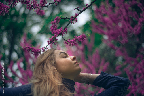 beautiful woman enjoying blooming oriental pink buds  mystical atmosphere  young woman looking up at the Cercis canadensis tree  blooming flowers concept of happiness and spring freshness