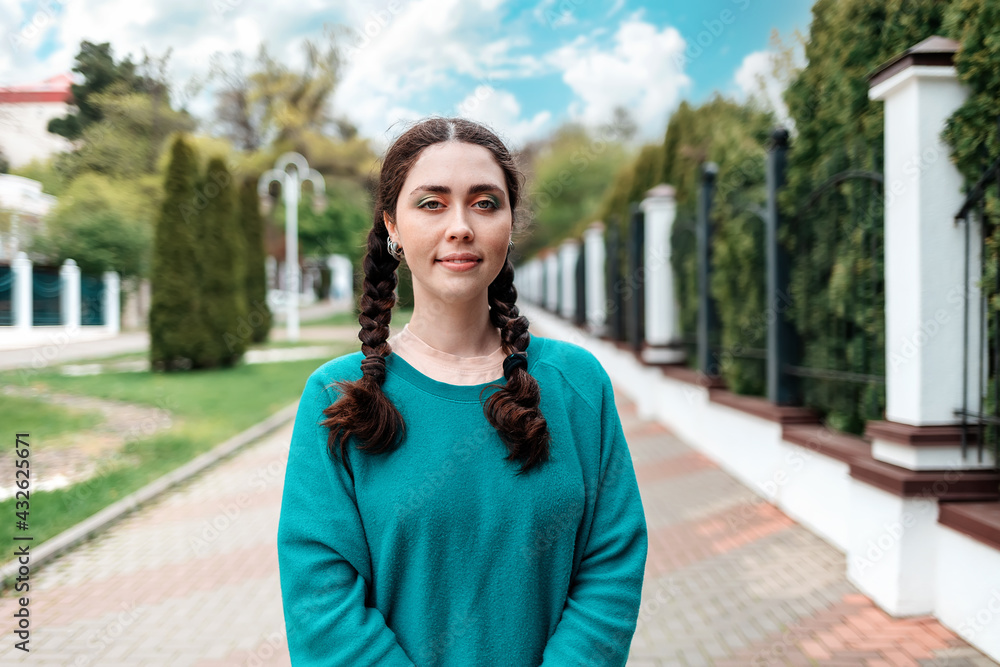 Portrait of young female student with pigtails stands on the street, at the entrance to the university. Outdoor, fence. The concept of admission of students to the university