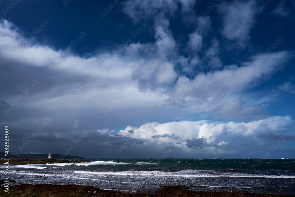 coastal lighthouse on sunny day with storm clouds on the horizon