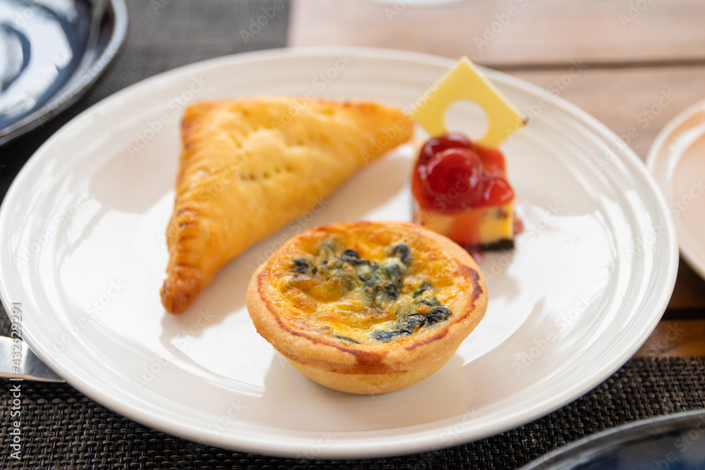 Spinach quiche, Pie and Cheesecake mini snack set on white plate in a garden. Spinach quiche, Pie and Cheesecake mini snack set on white plate in a garden.