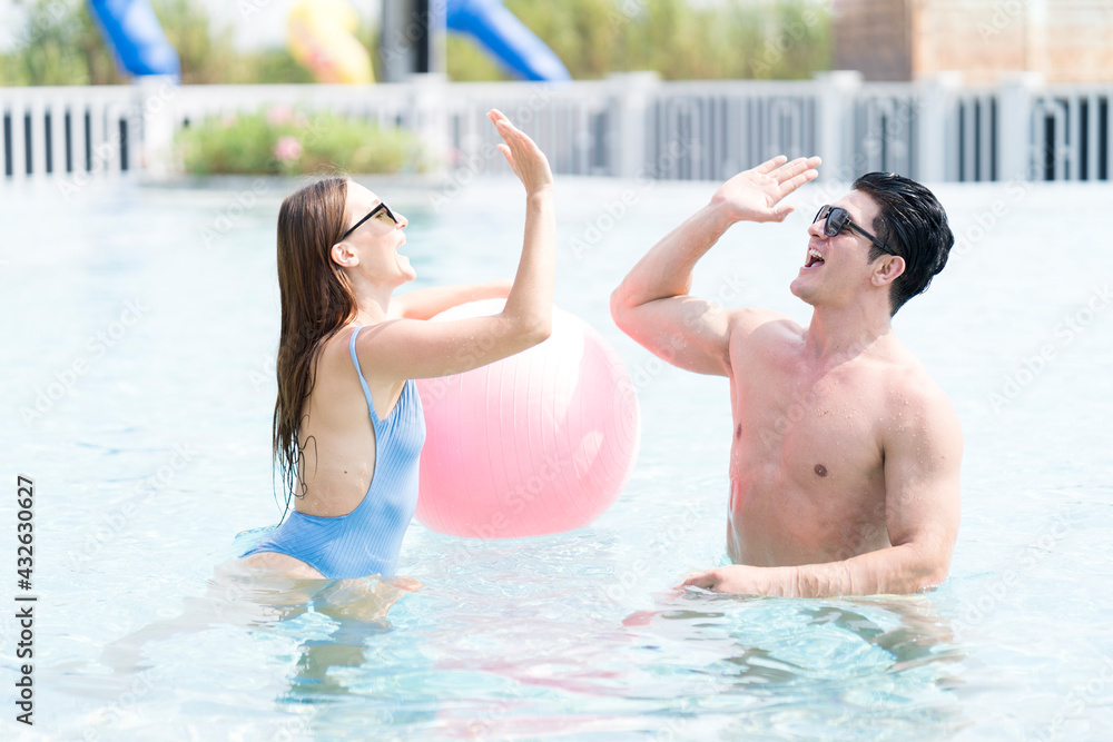 Happy couple and summer vacations at resort. Couple into swimming pool with their hand. Male and female playing in the pool with a beach ball.