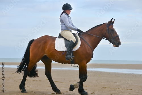Young woman lives her dream riding her beautiful bay horse on an empty beach in rural Wales.