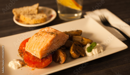 steamed sea trout fillet served on fried mushrooms with tomatoes on a white plate