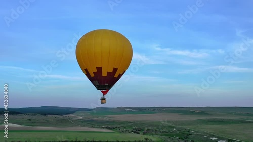 Yellow hot air balloon in the blue sky. Balloon flies over the trees. Beautiful romantic summer scene. aerial view