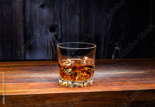 Fotografie Glass of whiskey with ice cubes on an oak wooden board.