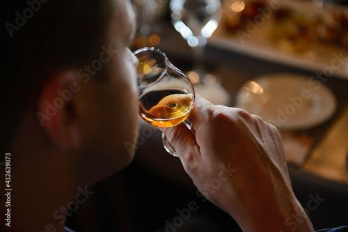 Photo Man holding glass of cognac close to nose smelling the aroma
