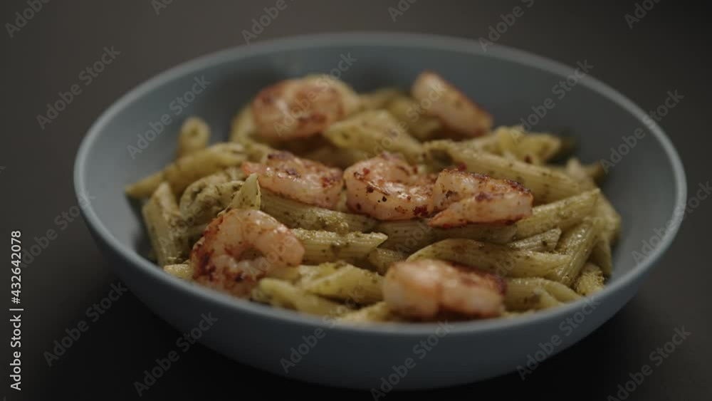 Slow motion handheld shot of pesto penne with fried shrimps in blue bowl on black background Slow motion handheld shot of pesto penne with fried shrimps in blue bowl on black background