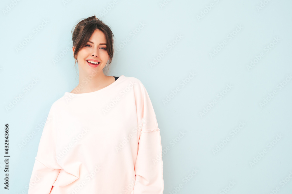 Portrait of young beautiful smiling female in trendy summer pink clothes. Sexy carefree woman sitting near light blue wall in studio. Positive model having fun indoors Portrait of young beautiful smiling female in trendy summer pink clothes. Sexy carefree woman sitting near light blue wall in studio. Positive model having fun indoors