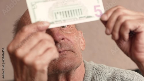 Close-up of a Caucasian pensioner examines a 5 dollar bill, holding it in front of his eyes. 5 dollar banknote in the hands of a man. selective focus, shallow depth of field photo