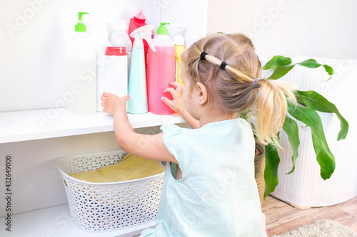 Toddler touches bottles of household chemicals  household cleaning products.