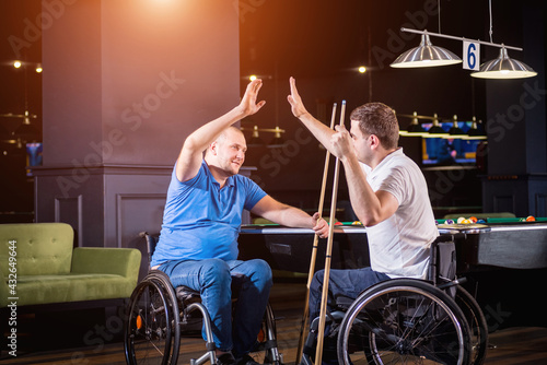 Adult men with disabilities in a wheelchair play billiards in the club