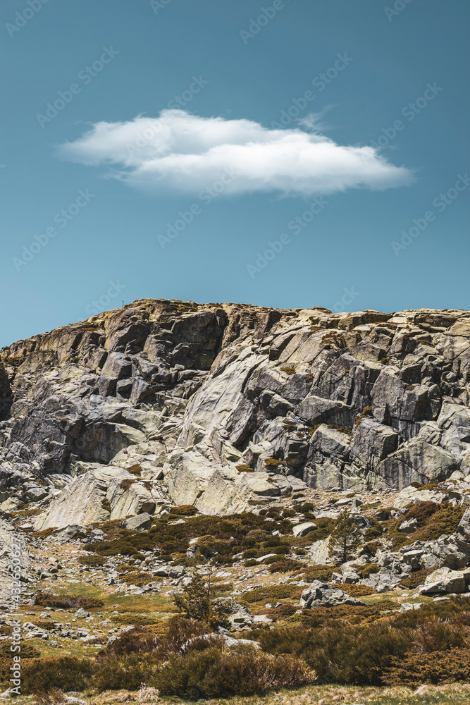 Top of a mountain seen from below with a large cloud in the sky.