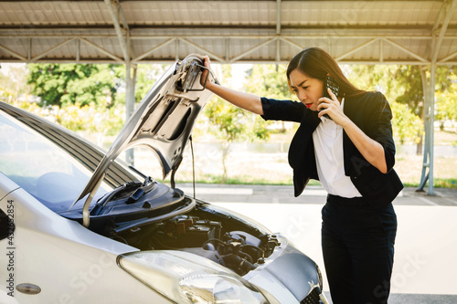 Businesswoman stand to look at the damaged engine while traveling, unable to drive and use the phone to find insurance for help in the parking lot.
 photo