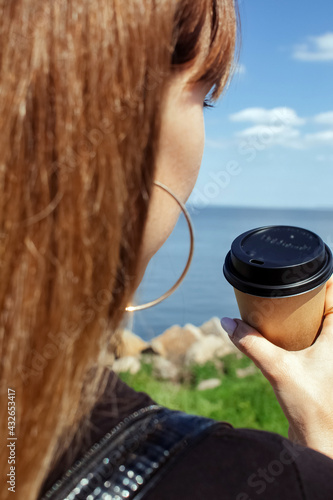 Girl holding coffee on a beautiful background. The concept of the beginning of the morning, vigor and environmental friendliness. Paper cup with takeaway coffee in hand. Vertical photo