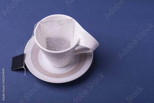 Tablou pe pânză Closeup shot of a single teabag inside a porcelain white cup on dark blue backgr