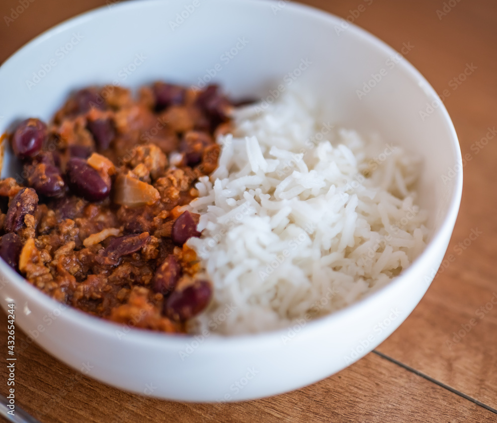 Close up and selective focus of meat chilli concarne and white rice in a white bowl on a wooden surface with intentional shallow depth of field and bokeh Close up and selective focus of meat chilli concarne and white rice in a white bowl on a wooden surface with intentional shallow depth of field and bokeh