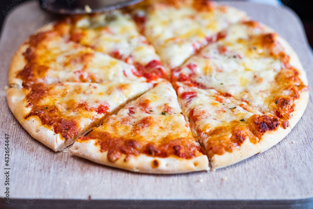 Close up and selective focus of a home cooked thin crust four cheese pizza cut in to slices on a wooden cutting board