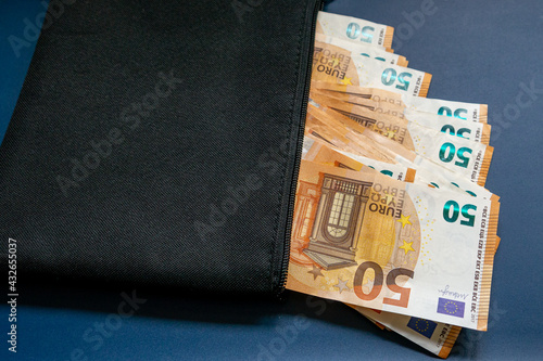 Schwarze Geldtasche mit einem Hundert Euro Schein und mehreren Fünfzig Euro Banknote, vor blauen Hintergrund photo