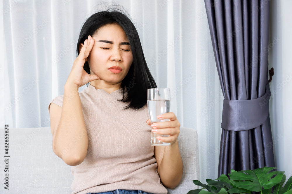 Asian woman suffering from headache after drinking cold water hand holding her head and glass of water Asian woman suffering from headache after drinking cold water hand holding her head and glass of water