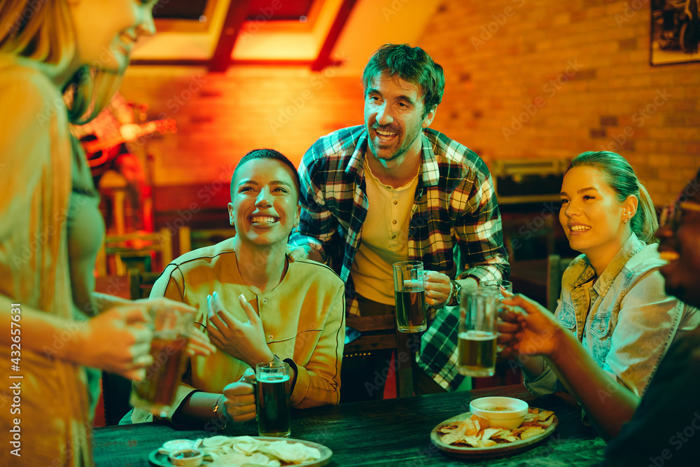 Group of young happy people drinking beer and having fun in a pub at night.