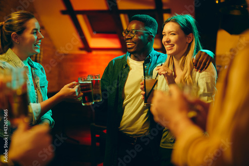 Young cheerful adult toasting while drinking during the night out in a pub.