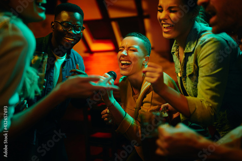 Group of happy friends singing karaoke during a night party at the pub. photo