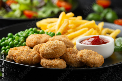 Fried crispy chicken nuggets with ketchup  french fries and green peas in black plate