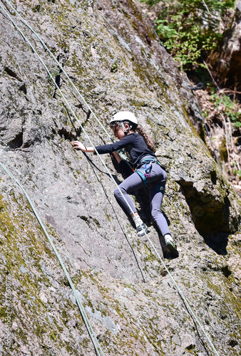 A young girl is climbing a rock. A girl with a rope engaged in the sports of rock climbing on the rock.